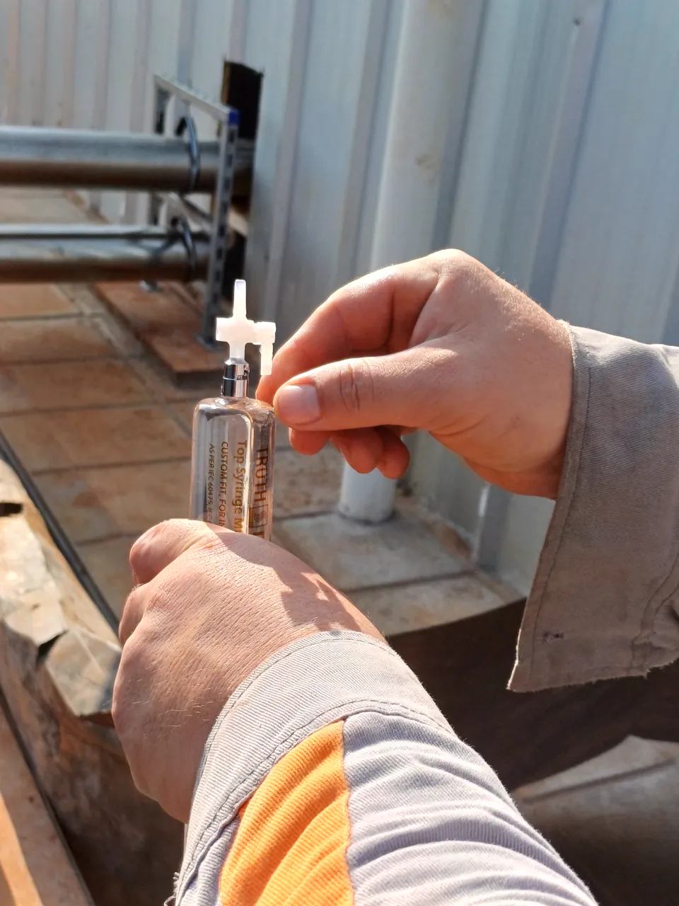 Hands collecting an oil sample from a transformer using a glass syringe