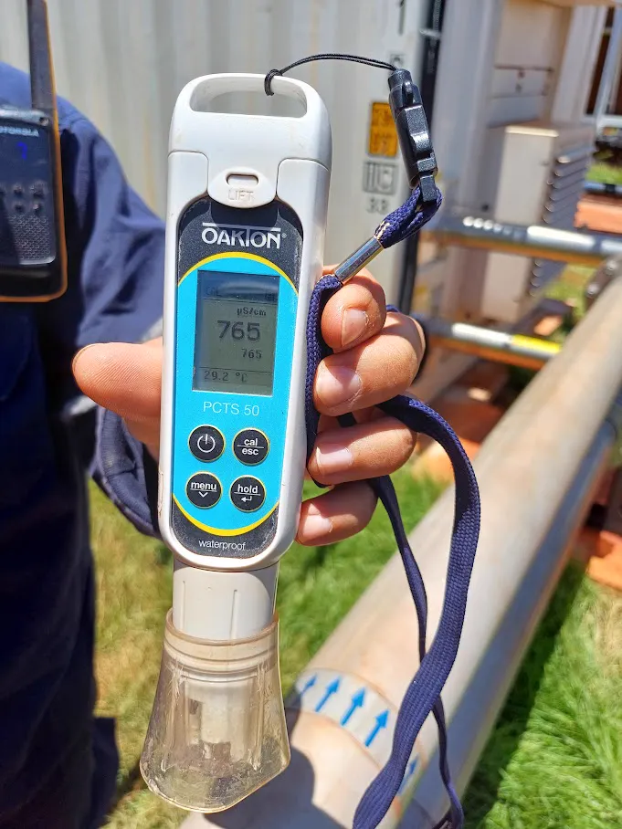 Handheld water conductivity meter reading next to a cooling pipe